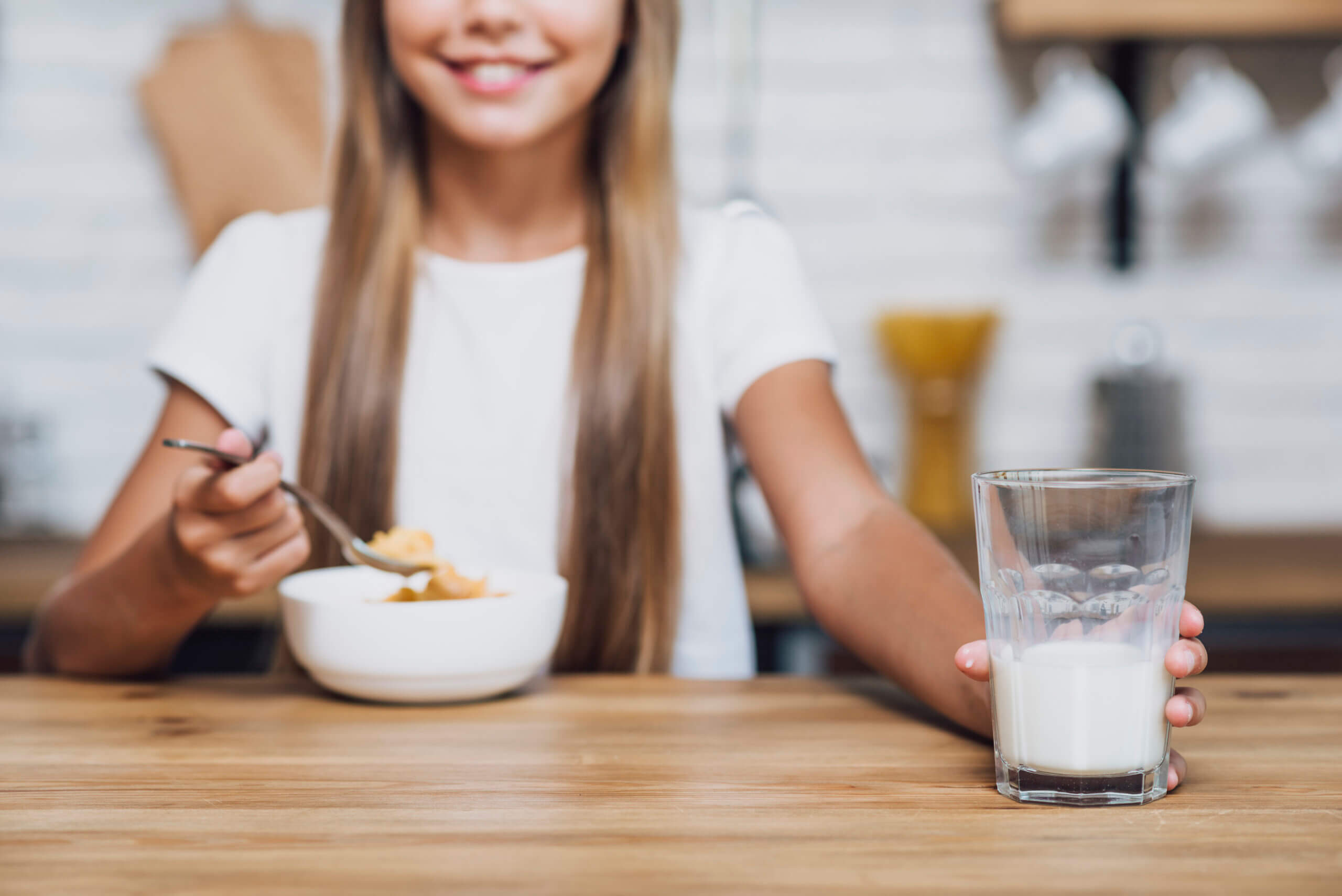 menina sorridente, segurando um copo de leite enquanto come cereais