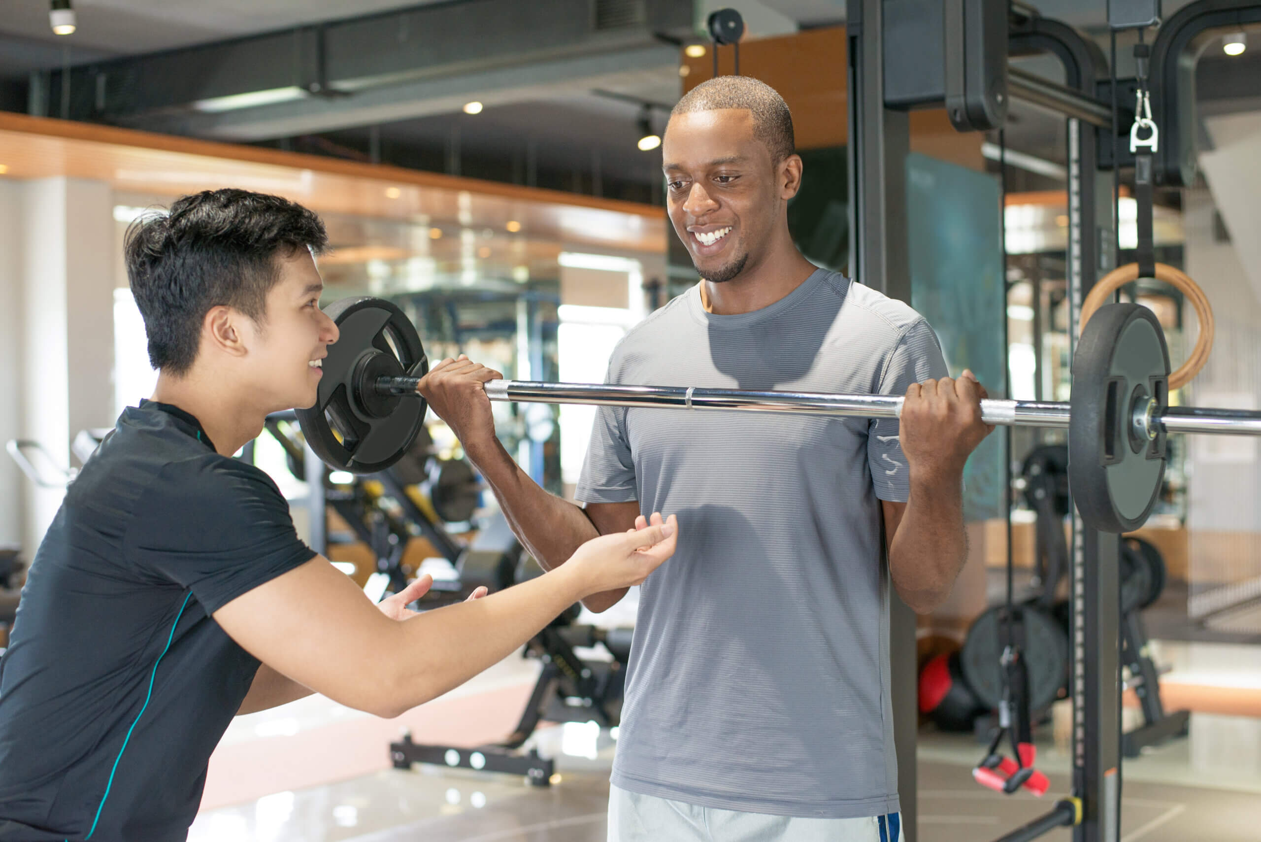homem negro sorridente, levantando a barra com personal trainer
