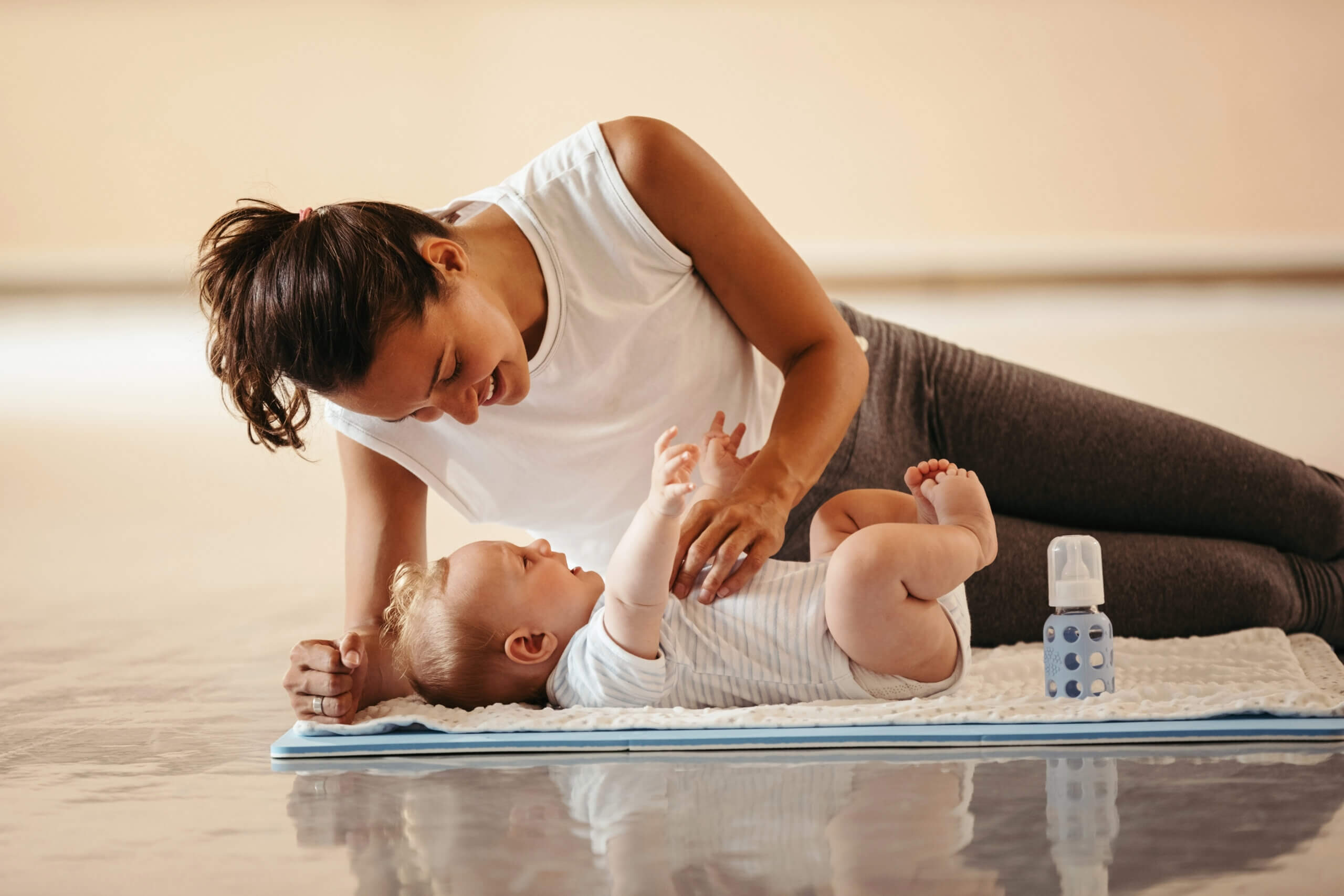 mãe atlética brincando com seu filho que está deitado no colchonete no health club